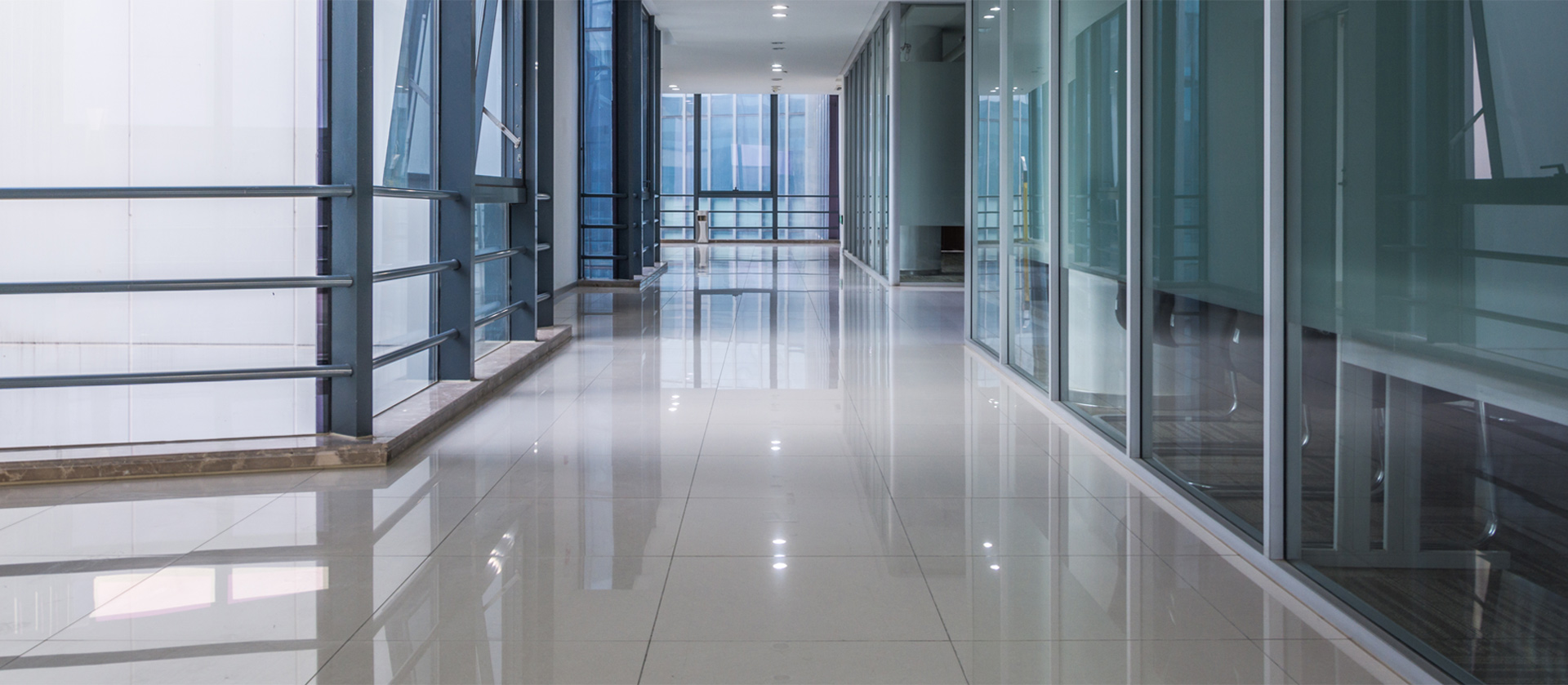 A long hallway with glass walls and white tile floors.